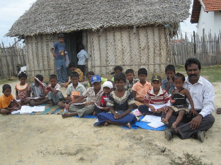 Children and adults gathered outdoors with books and learning materials